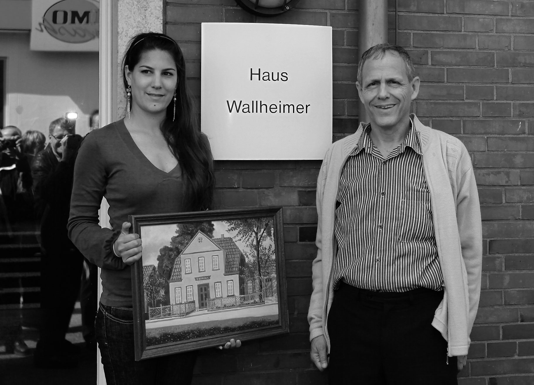 Berni Wallheimers Sohn Nir mit Tochter Adina in Aurich vor dem Haus am Breiten Weg 1. Adina hält ein Bild vom Haus.